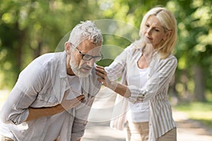 Senior man suffering from heart attack while walking with wife in park