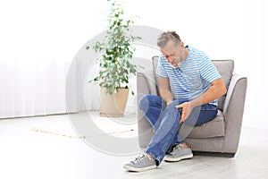 Senior man suffering from knee pain in living room.