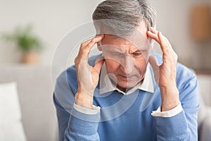 Senior Man Suffering From Migraine Sitting On Sofa At Home
