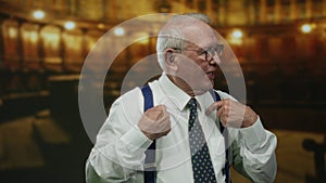 Senior man in a suit gestures confidently while speaking inside a dimly lit church, emphasizing his points with expressive hand