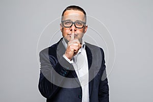 Senior man in suit gesturing silence, standing on white