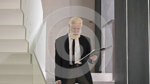 Senior man in suite with notepad going downstairs in a building