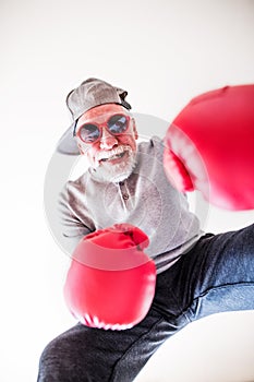 A senior man with sunglasses and boxing gloves having fun at home.