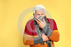 Senior man suppressing cough on yellow background. Cold symptoms