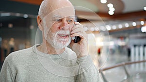 Senior man in sweater in mall use mobile phone. Male shopper in shopping center talking on cellphone