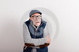 Senior man in sweater, vest jacket and cap, studio shot.