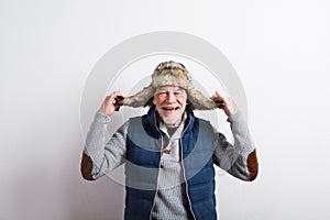 Senior man in sweater, vest jacket and fur hat, studio shot.