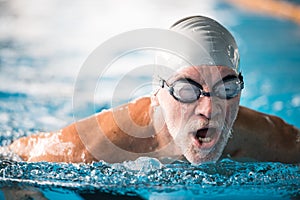 Senior man swimming in an indoor swimming pool.