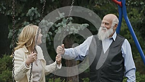 Senior man swings a young woman on seesaw in slowmotion