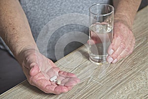 Senior man at table with medication in hand and glass of water