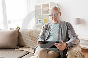 Senior man with tablet pc sitting on sofa at home