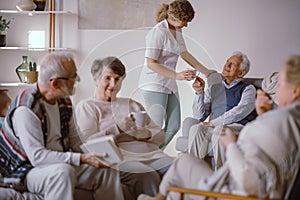 Senior man taking a cup of tea from his caregiver in the nursing home