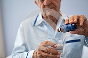 Senior man taking medicine drop at hospital