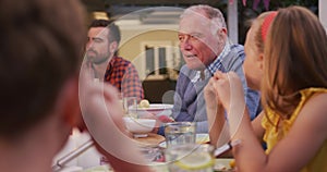 Senior man taking to family members while having dinner outdoors