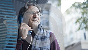 Senior man talking on public payphone in outdoors