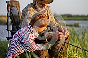 Senior man teach grandson how to put a worm on fishing hook, close-up, side view