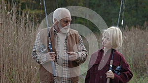 Senior man and teen boy walking on nature with fishing rods