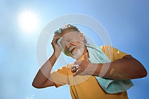 Senior man with towel suffering from heat stroke outdoors, low angle view