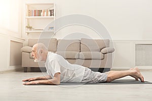 Senior man training yoga in cobra pose indoors