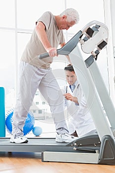 Senior man on treadmill with therapist crouching