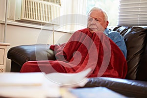 Senior Man Trying To Keep Warm Under Blanket At Home