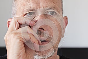 Senior man with unshaved stubble beard picking his nose. Thumb up in his nostril.