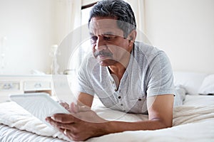 Senior man using digital tablet on bed