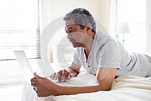Senior man using digital tablet on bed