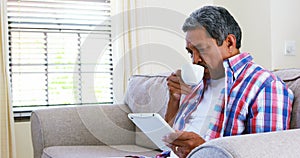 Senior man using digital tablet while having coffee in living room 4k