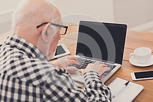 Senior man using laptop with blank screen mockup