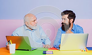 Senior man using a laptop computer with his son. Mature senior dad and young man sitting in office. Businessmen using