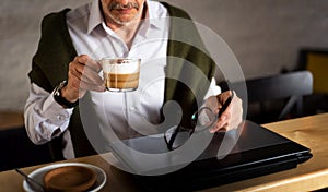 Senior man using laptop and having coffee in the bar