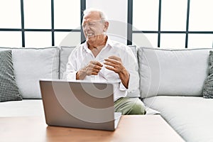 Senior man using laptop at home sitting on the sofa disgusted expression, displeased and fearful doing disgust face because