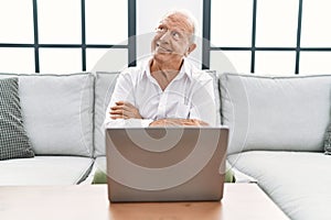 Senior man using laptop at home sitting on the sofa smiling looking to the side and staring away thinking