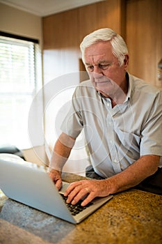 Senior man using laptop in the kitchen