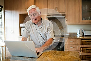 Senior man using laptop in the kitchen