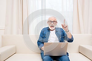 Senior man using laptop and pointing up with finger