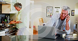 Senior man using laptop while woman cooking in background 4k