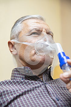 Senior man using medical equipment for inhalation with respiratory mask, nebulizer