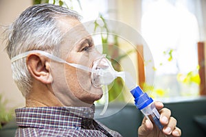 Senior man using medical equipment for inhalation with respiratory mask, nebulizer