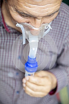 Senior man using medical equipment for inhalation with respiratory mask, nebulizer