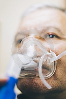 Senior man using medical equipment for inhalation with respiratory mask, nebulizer