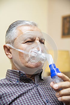 Senior man using medical equipment for inhalation with respiratory mask, nebulizer