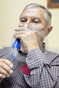 Senior man using medical equipment for inhalation with respiratory mask, nebulizer