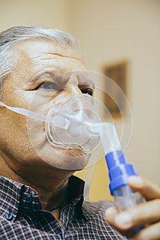 Senior man using medical equipment for inhalation with respiratory mask, nebulizer