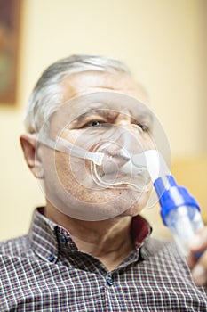 Senior man using medical equipment for inhalation with respiratory mask, nebulizer