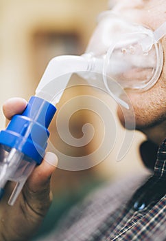 Senior man using medical equipment for inhalation with respiratory mask, nebulizer