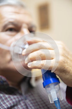 Senior man using medical equipment for inhalation with respiratory mask, nebulizer