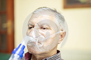 Senior man using medical equipment for inhalation with respiratory mask, nebulizer