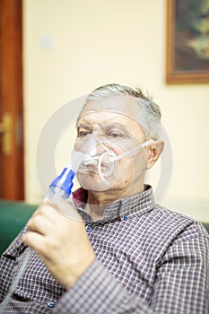 Senior man using medical equipment for inhalation with respiratory mask, nebulizer